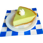 slice of key lime pie with whip cream on a white plate on a blue and white checker paper
