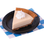 Slice of Key Lime pie with a dollop of whipped cream. On a small black plate placed on a white and blue checkered paper