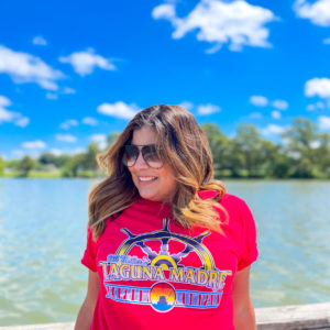 Laguna Madre employee wearing red t-shirt with logo and wheel in front of lake