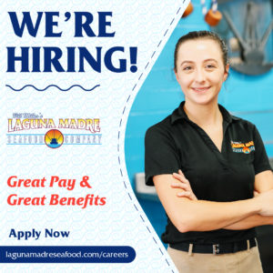 We're Hiring! Great Pay & Great Benefits. Apply now button; Laguna Madre manager Ziane Olson in Laguna Madre uniform with arms crossed and smile on her face in dinning room. Background includes waves and dashes.Laguna Madre logo.